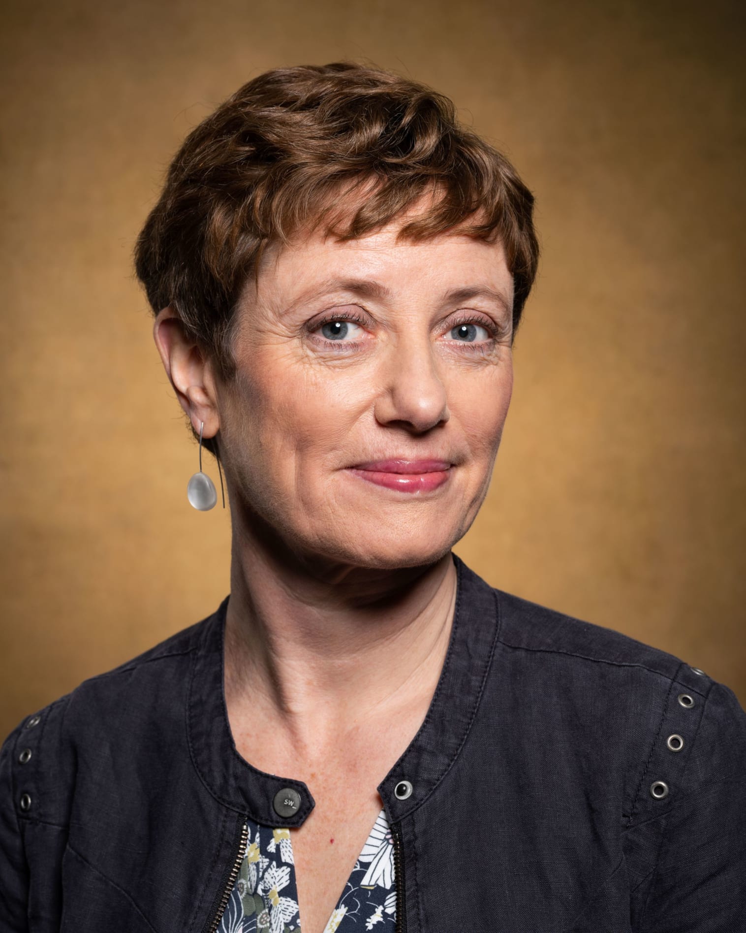 This is a photograph of Rebecca Lunn. She has short, brown hair, is wearing a navy jacket and pictured against a beige background.